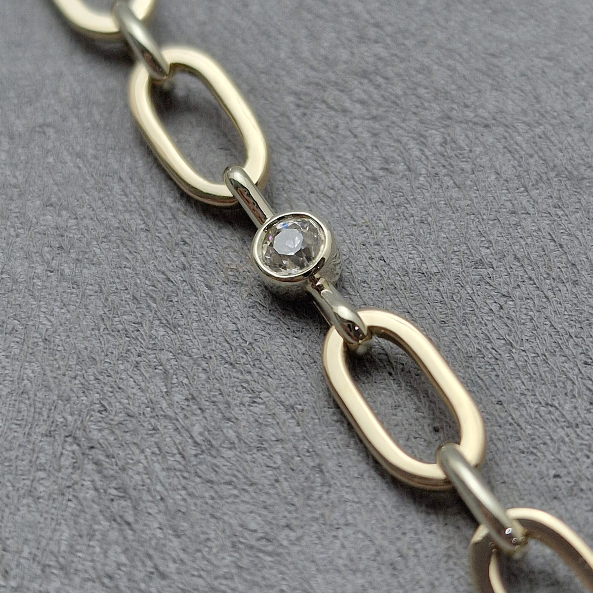 A close-up of a 9ct yellow and white gold hand made chain link bracelet featuring a central oval link with a bezel-set diamond, remodelled from a watch and ring. Golden Snowdrop Shaftesbury.