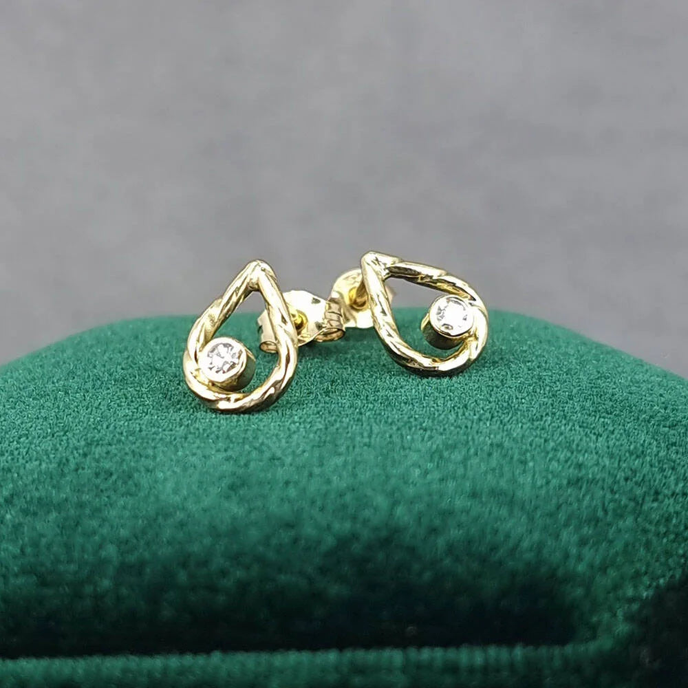 Gold Diamond Raindrop Stud Earrings earrings on a green cushion against a gray background