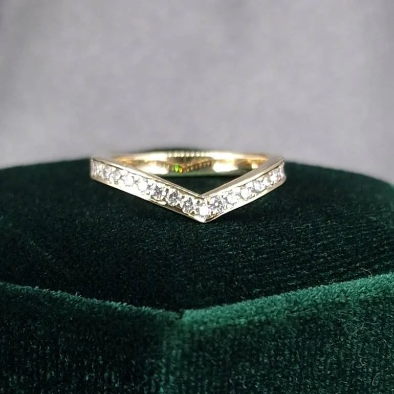 Gold ring with diamonds on a green cushion against a gray background