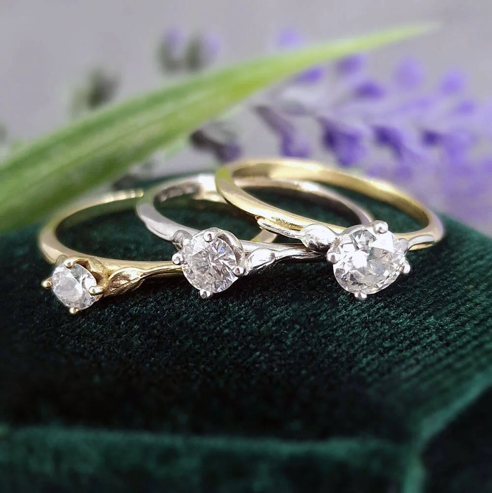 Three gold and silver rings with diamond-like stones on a green surface with blurred background